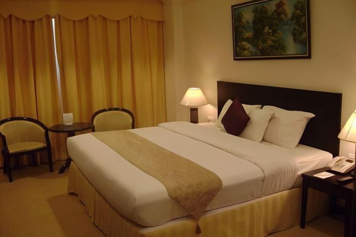 A hotel room with a large bed, two bedside tables, a chair, and a painting on the wall.