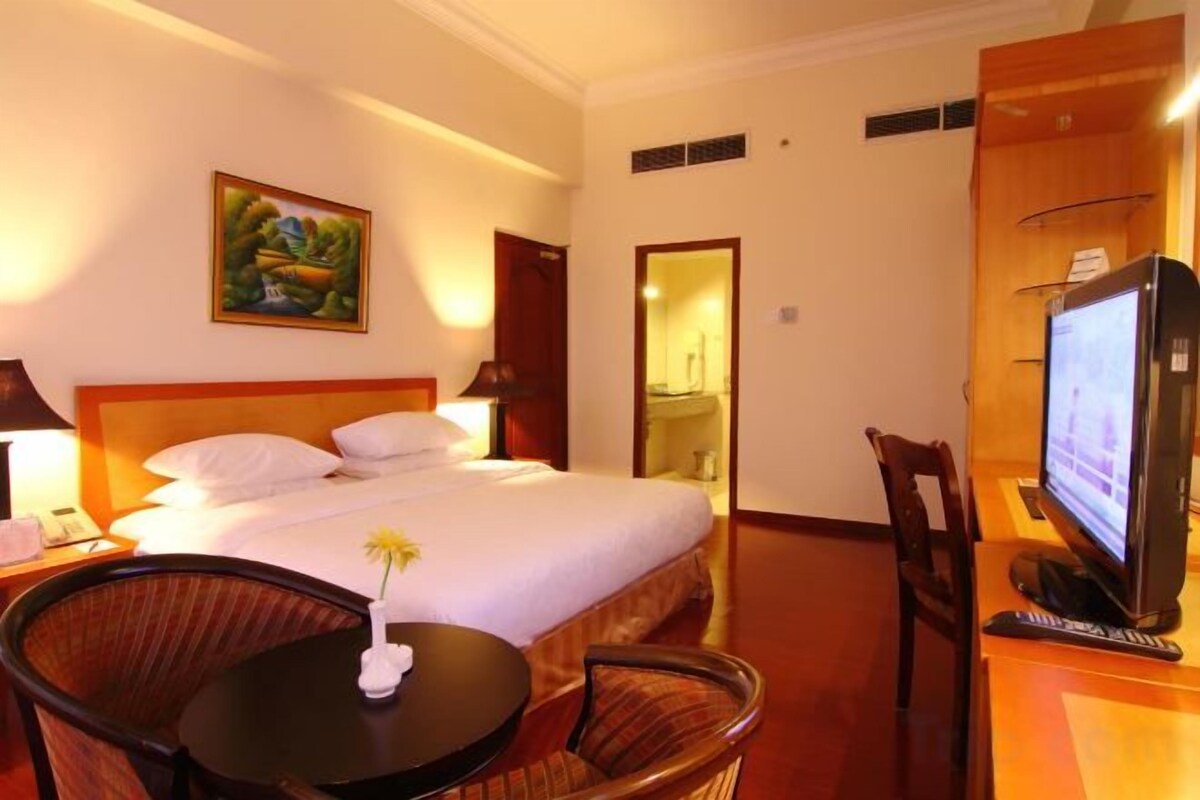 A hotel room with a bed, a television, a small table with a flower, and a chair.