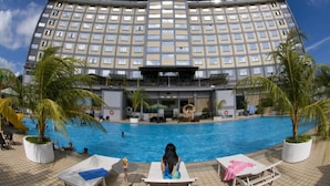 A hotel with a swimming pool, palm trees, and a large building facade.