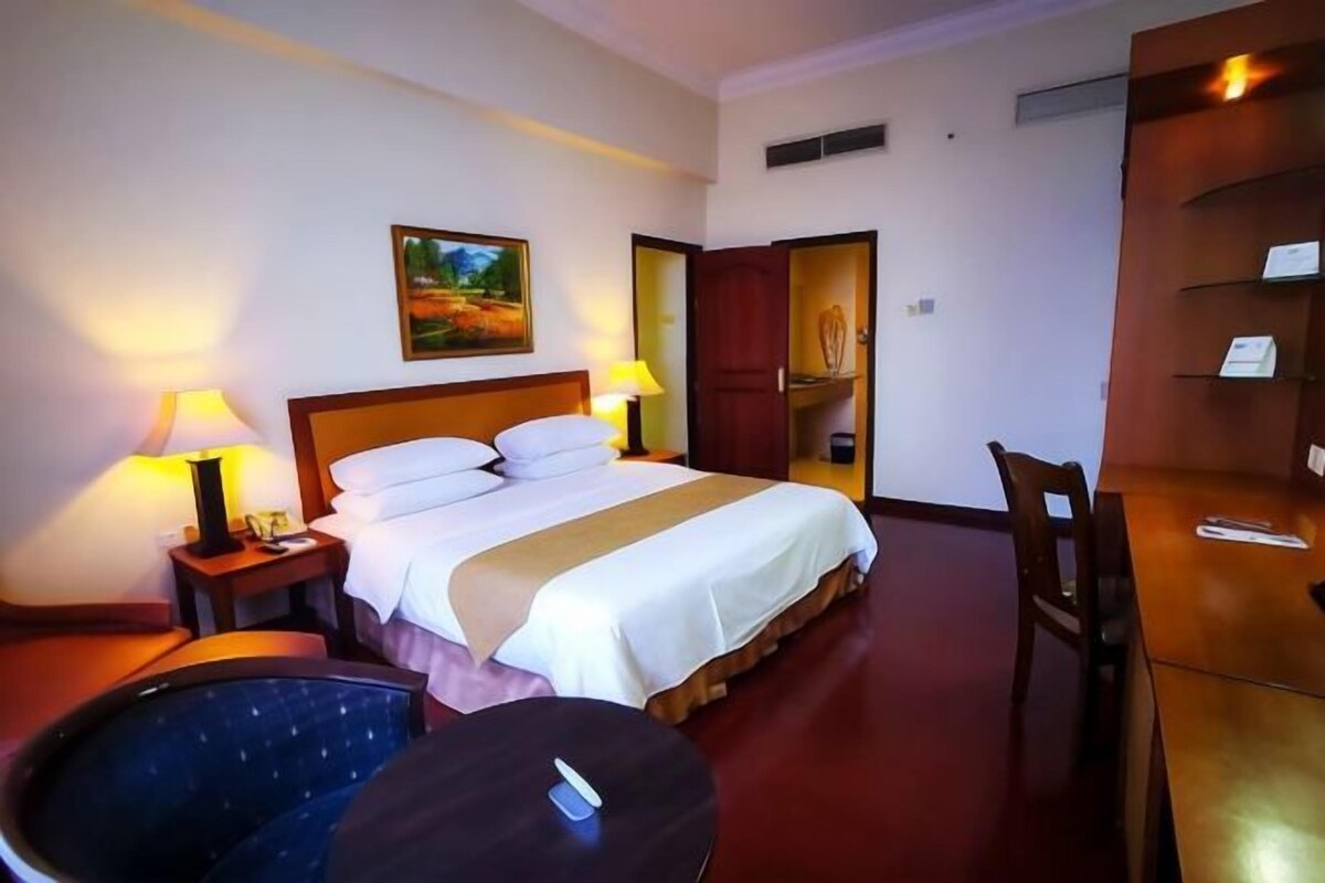 Une chambre d’hôtel avec un lit, des lampes de chevet, un bureau, une chaise et un tableau au mur.
