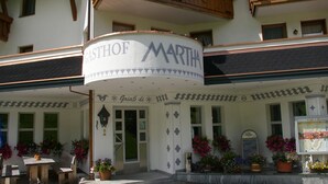 A building with a sign reading "GASTHOF MARTHA" and a cafe sign. There are flower pots and a bench outside. - Gasthof Martha (Nauders)