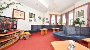 A living room with a blue sofa, a television, and a wooden coffee table. There are framed pictures on the walls and a plant on the windowsill. - Gasthof Martha (Nauders)