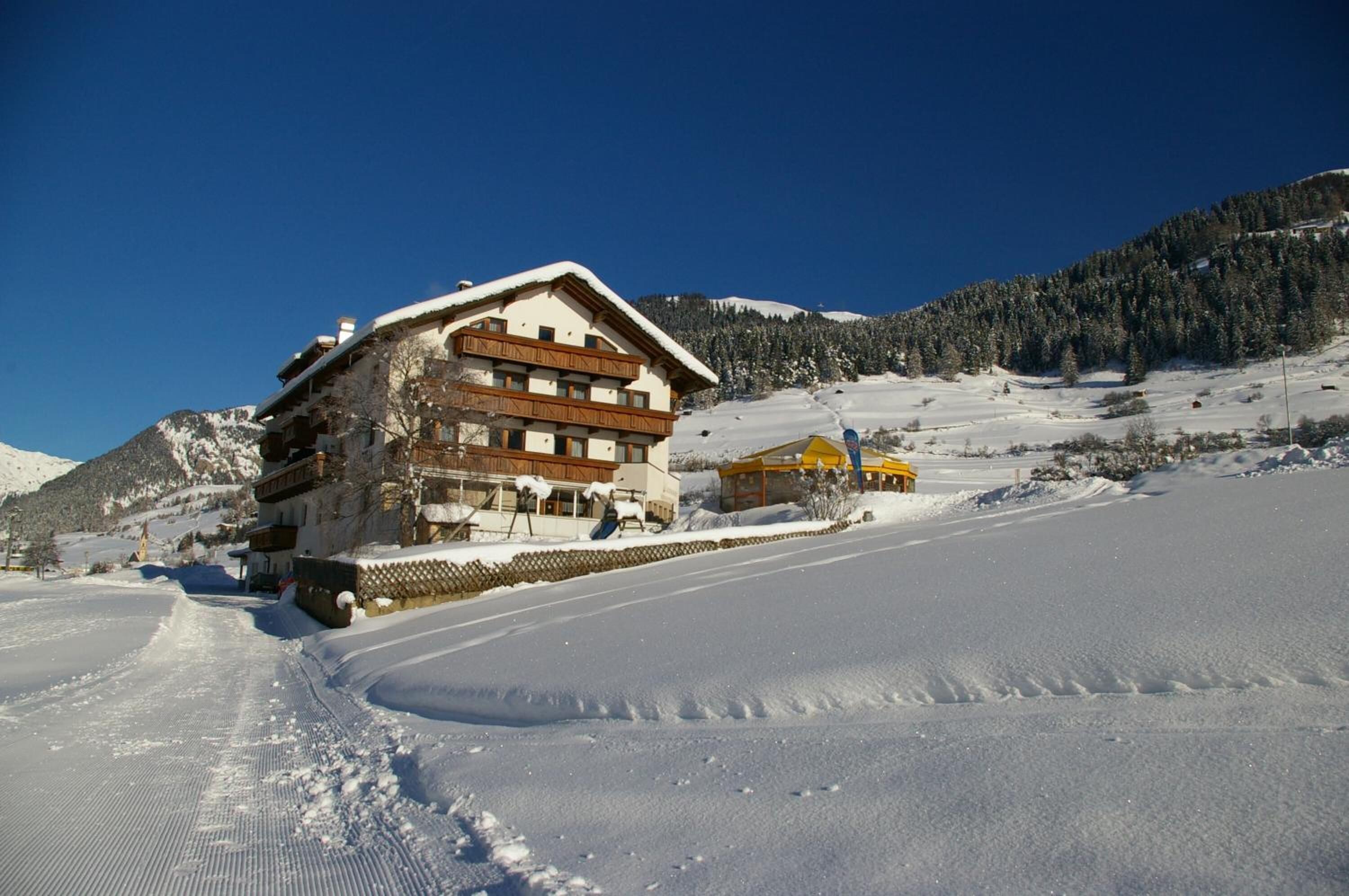 A snow-covered lodge with a wooden exterior and a sloped roof, situated on a snow-covered slope with a clear sky.