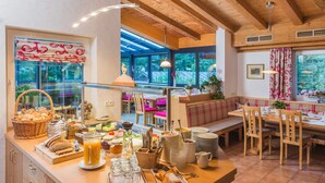 A breakfast buffet with a variety of food items and drinks, wooden furniture, and large windows with a view of the outdoors. - Hotel Pension Heike (Aurach bei Kitzbuehel)