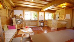 A cozy wooden cabin interior with a sofa, a table with a fruit bowl, a desk, and a reception area. - Hotel Pension Heike (Aurach bei Kitzbuehel)