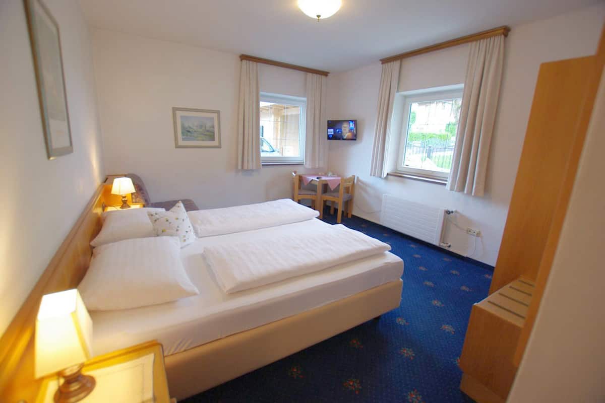 A hotel room with two beds, a desk, a chair, a TV, and a window with curtains.