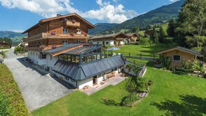 A large wooden chalet with a balcony, a covered patio, and a view of the surrounding countryside. - Hotel Pension Heike (Aurach bei Kitzbuehel)