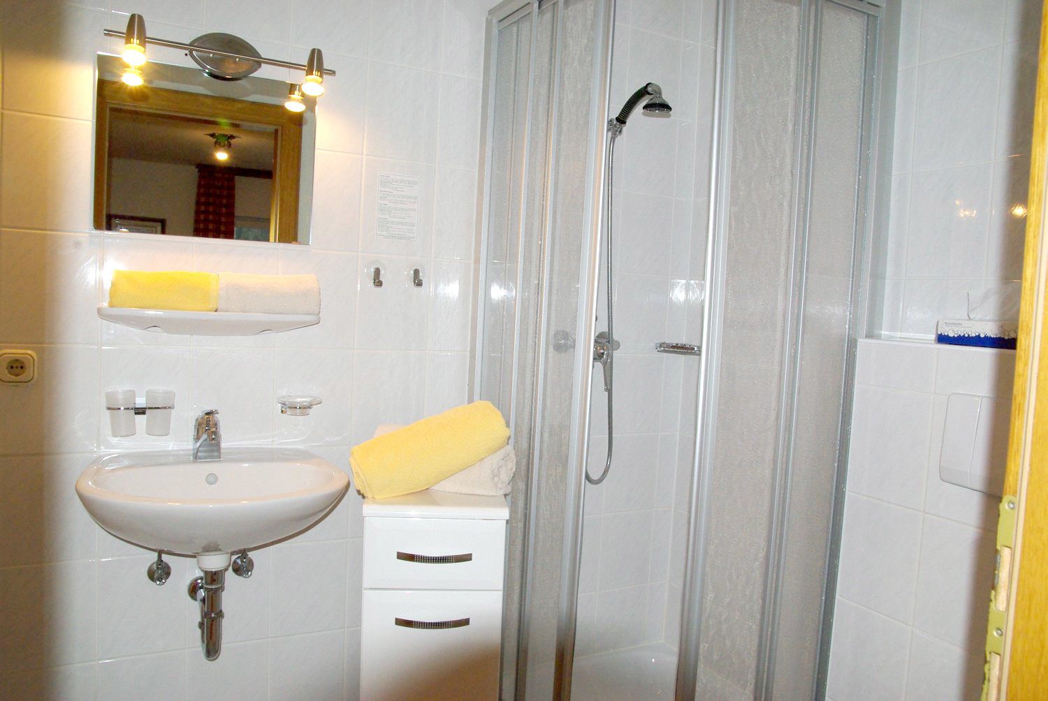 A bathroom with a sink, mirror, towel rack, and a shower enclosure.