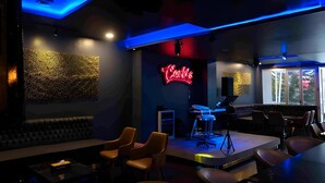 A modern bar area with a neon sign, seating, and a stage with musical equipment. - Splash Hotel Bengkulu (BENGKULU)