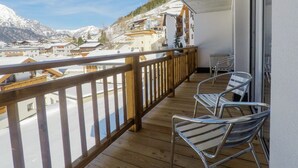 A balcony with wooden railings and metal chairs, overlooking a snowy mountain landscape with buildings. - Collina Hotel Garni (Nauders)