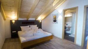 A bedroom with a wooden ceiling, a bed with white linens, a nightstand, and a wall-mounted light. - Collina Hotel Garni (Nauders)