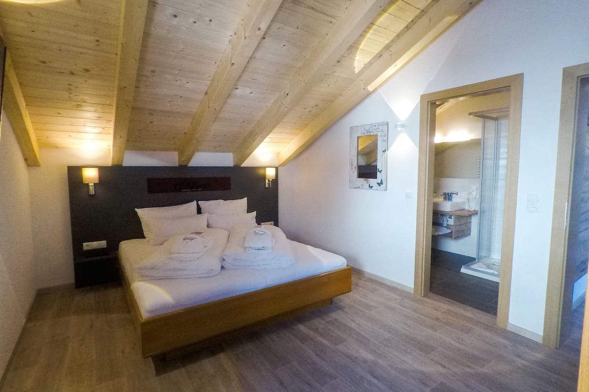 Ein Schlafzimmer mit Holzboden, einem Bett mit weißen Bettwäsche, einem Nachttisch und einer Wandleuchte.