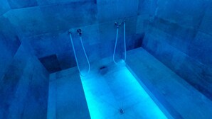 A blue-lit room with a bathtub, a shower, and a drain. - Collina Hotel Garni (Nauders)