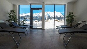 A room with two lounge chairs facing a large window with a mountain view. - Collina Hotel Garni (Nauders)