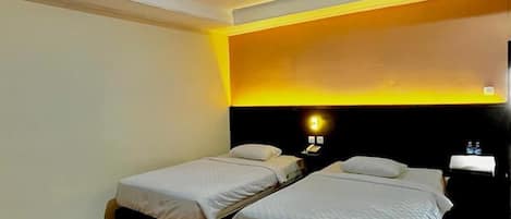Une chambre d’hôtel avec deux lits simples, une table de chevet avec une lampe et un luminaire au plafond.