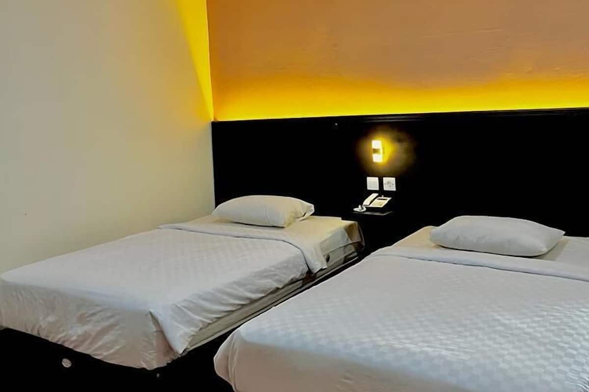 A hotel room with two single beds, a black headboard, a ceiling light, and a wall-mounted phone.