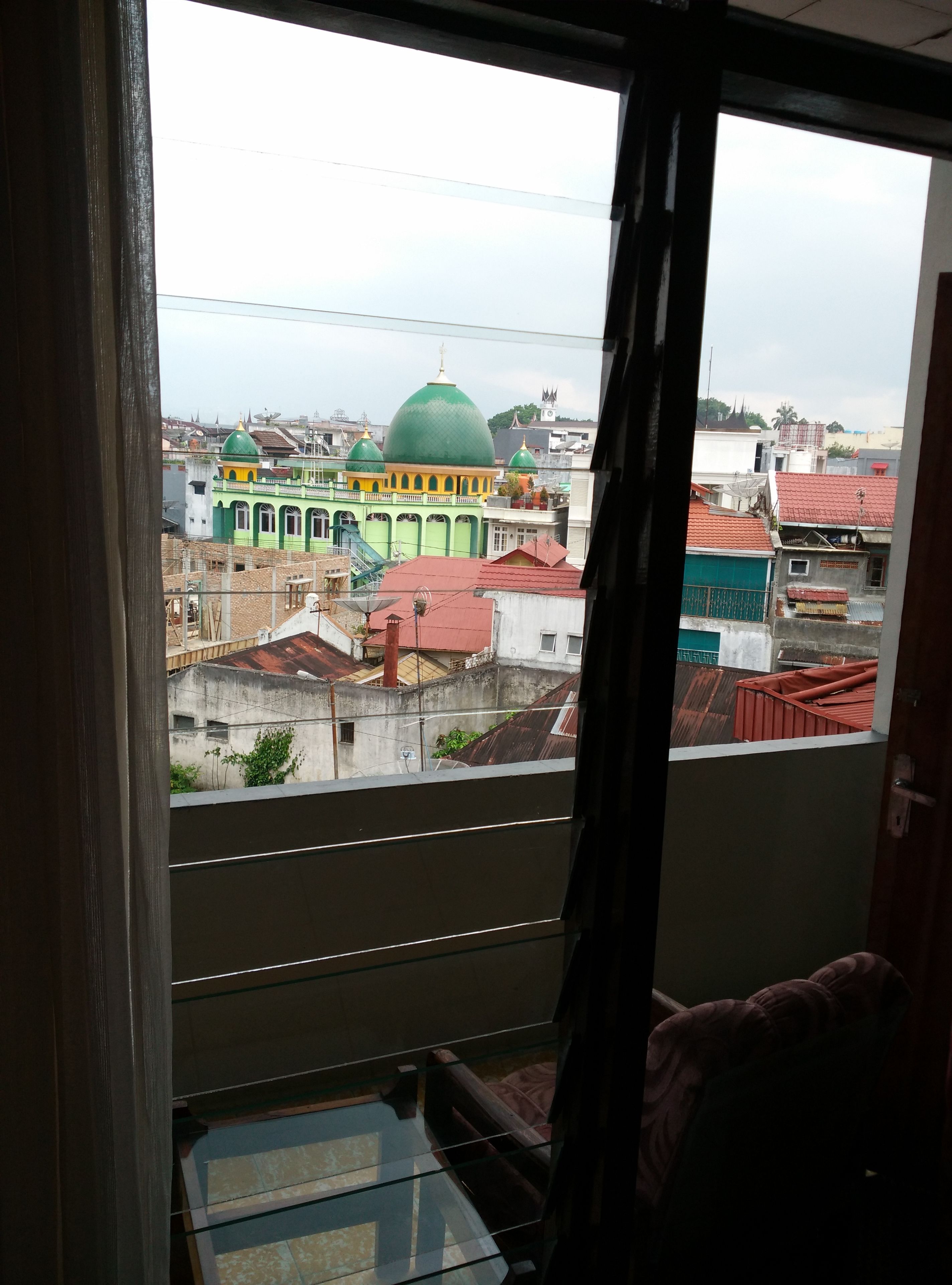 A view from a balcony with a glass floor, overlooking a cityscape with colorful buildings and a prominent green-domed structure.