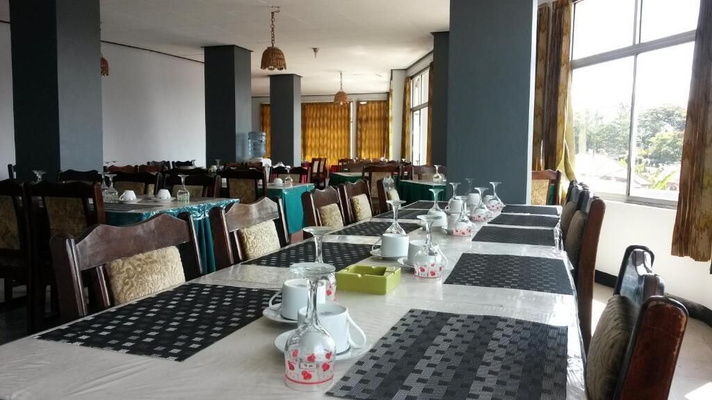 A dining area with tables set for service, chairs, and a view of the outdoors through large windows.