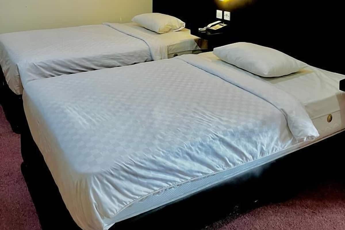 A hotel room with two beds, a nightstand with a lamp, and a dark headboard.