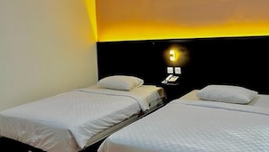 Et hotelværelse med to enkeltsenge, en mørk sengegavl og en vægmonteret lampe.