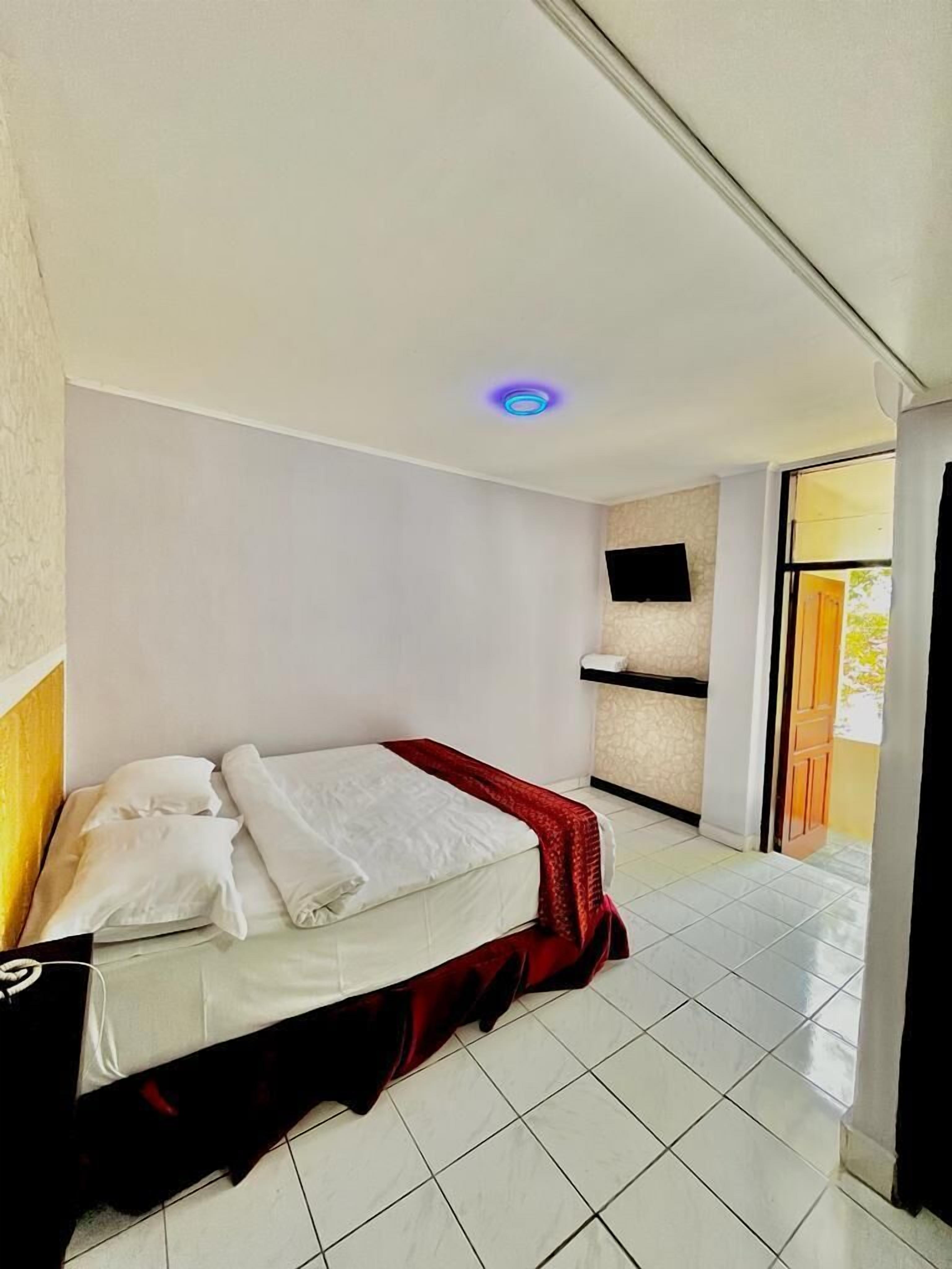 Habitación de hotel con una cama, un televisor de pantalla plana montado en la pared y una puerta corrediza de vidrio que da a un espacio al aire libre.
