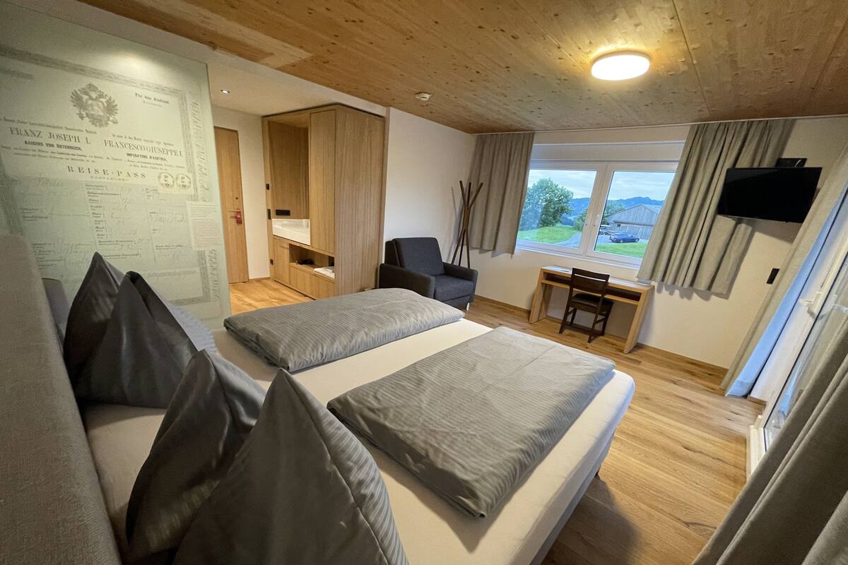 A room with two beds, a desk, a chair, a TV, and a window with a view of the outdoors.