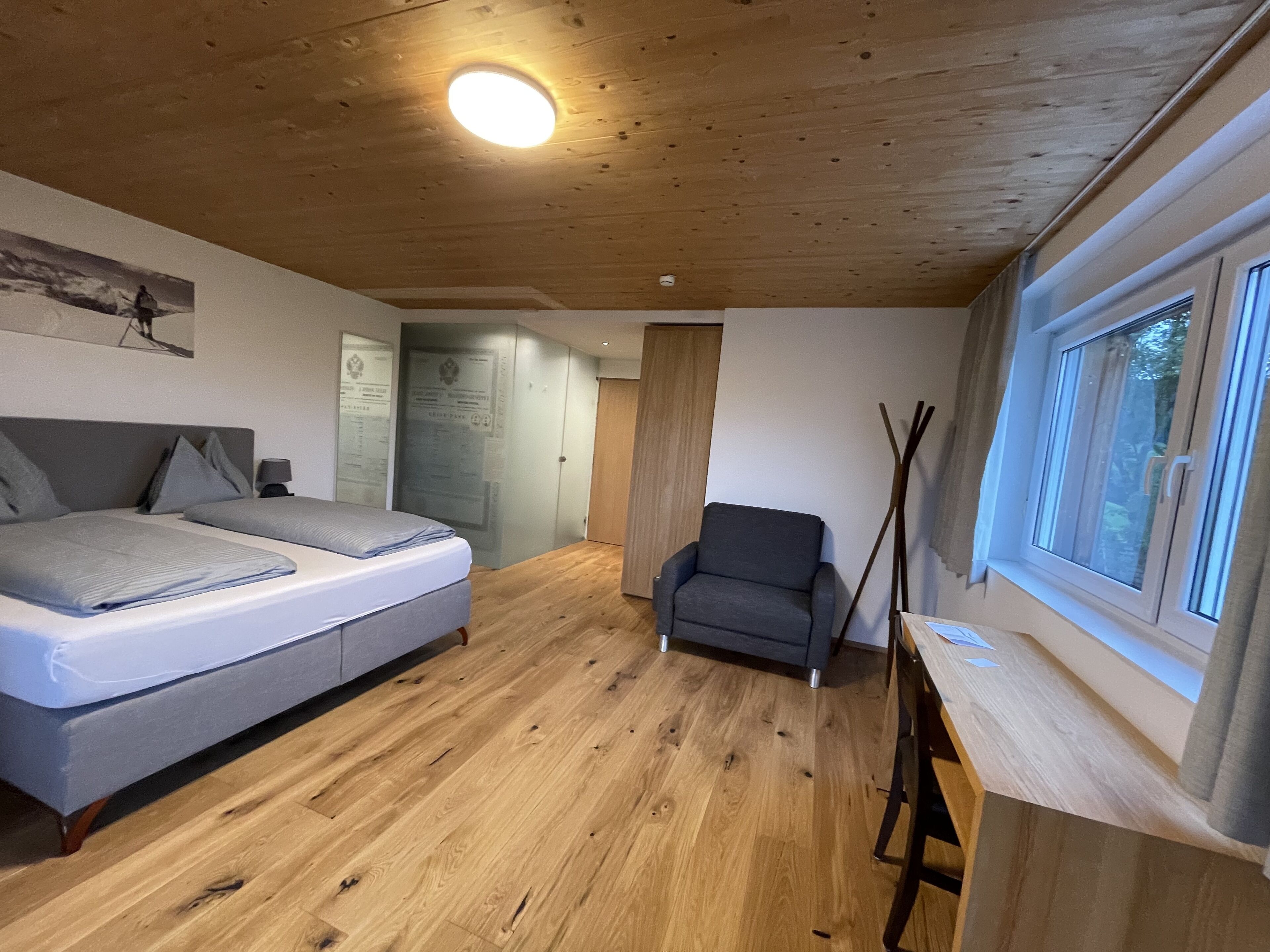 A bedroom with a bed, a chair, a desk, and a window.