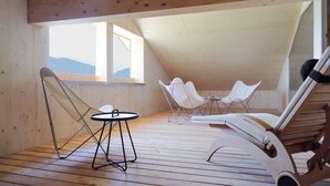 Un interior de madera con techo inclinado, sillas blancas, una pequeña mesa redonda y vistas al exterior.