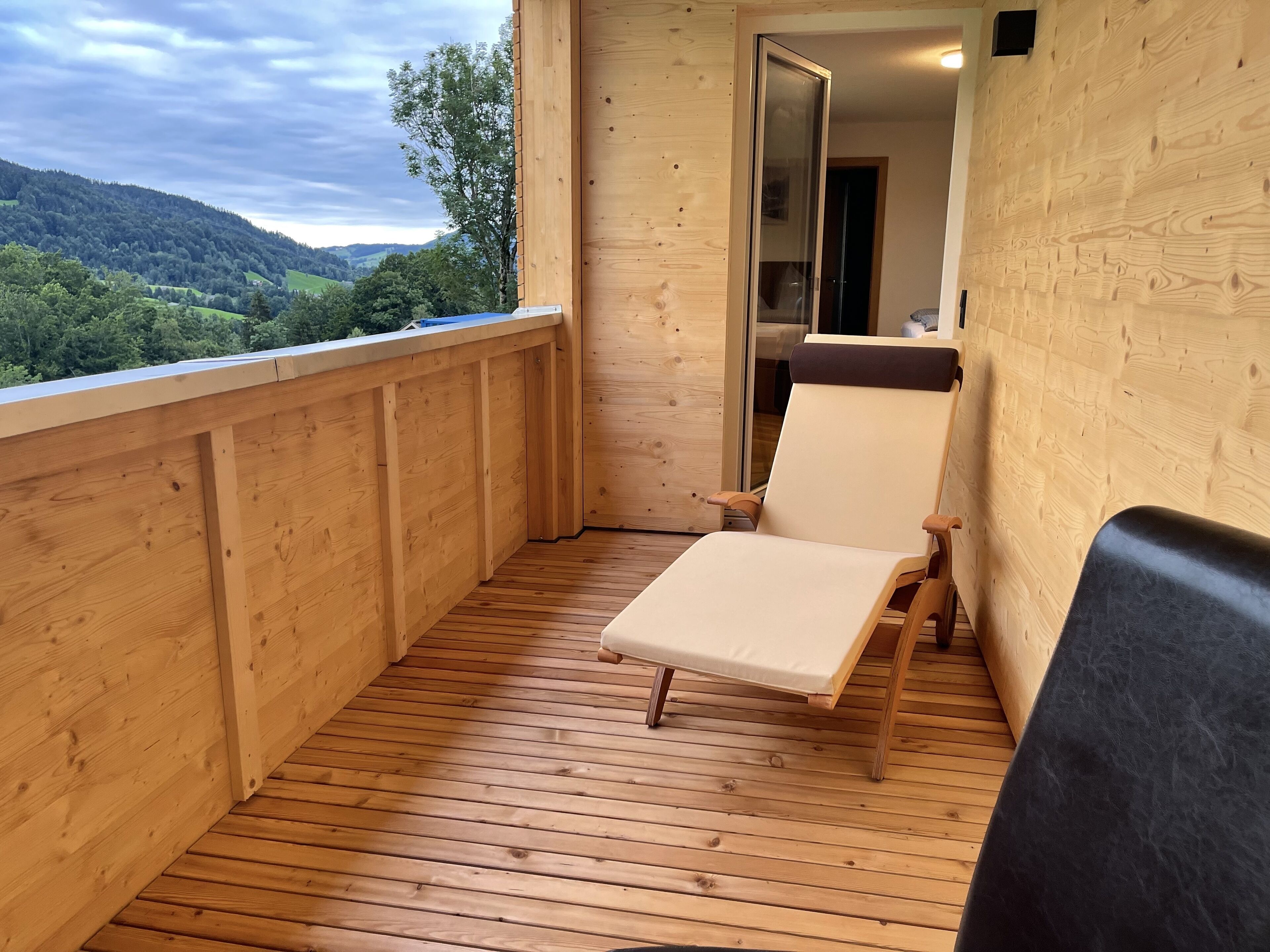 Um deck de madeira com uma única cadeira de descanso e vista para uma encosta arborizada.