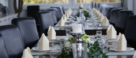 Una larga mesa de comedor dispuesta con servilletas blancas, copas transparentes y un centro de mesa con follaje.