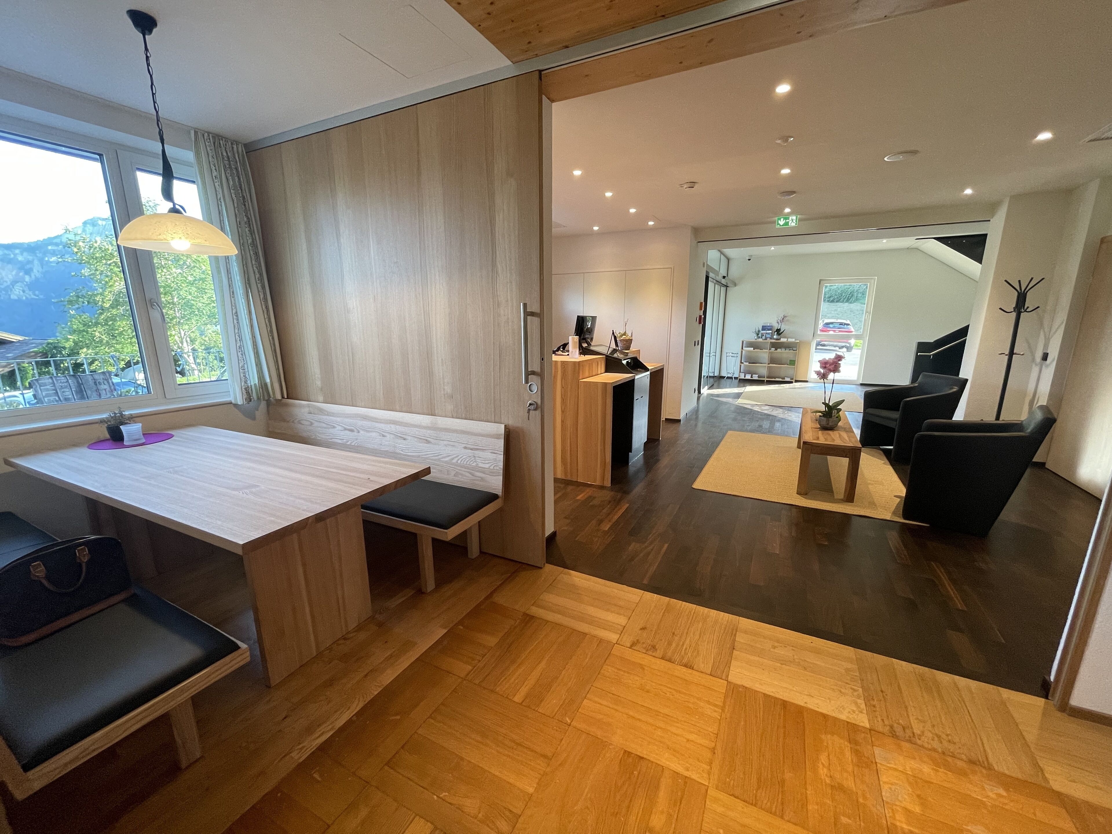 Un hall d’hôtel moderne avec un comptoir d’accueil en bois, un espace salon et une vue sur l’extérieur.