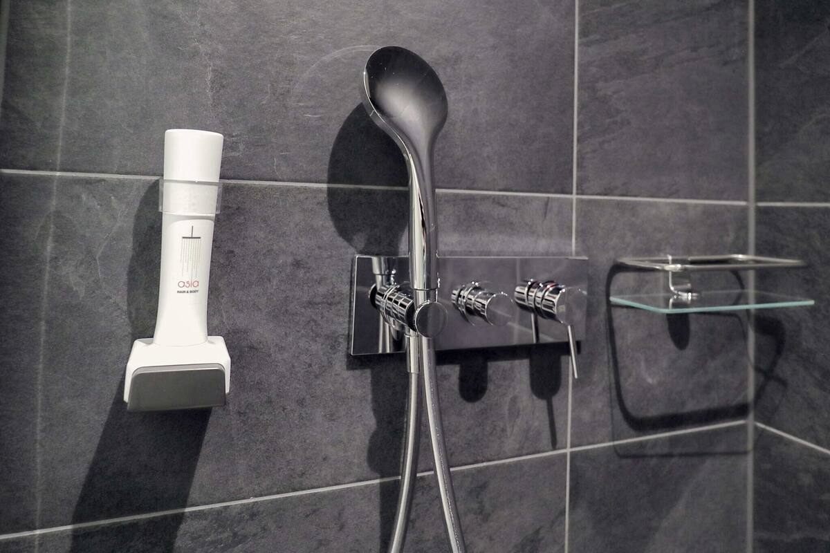 A bathroom with a modern shower system, including a handheld showerhead and a wall-mounted control panel.