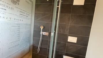 Une salle de bain avec une douche à parois de verre, des murs recouverts de carreaux foncés et des toilettes blanches.