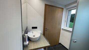 Un baño moderno con puerta de madera, lavamanos de cristal y ventana con vistas a la vegetación.