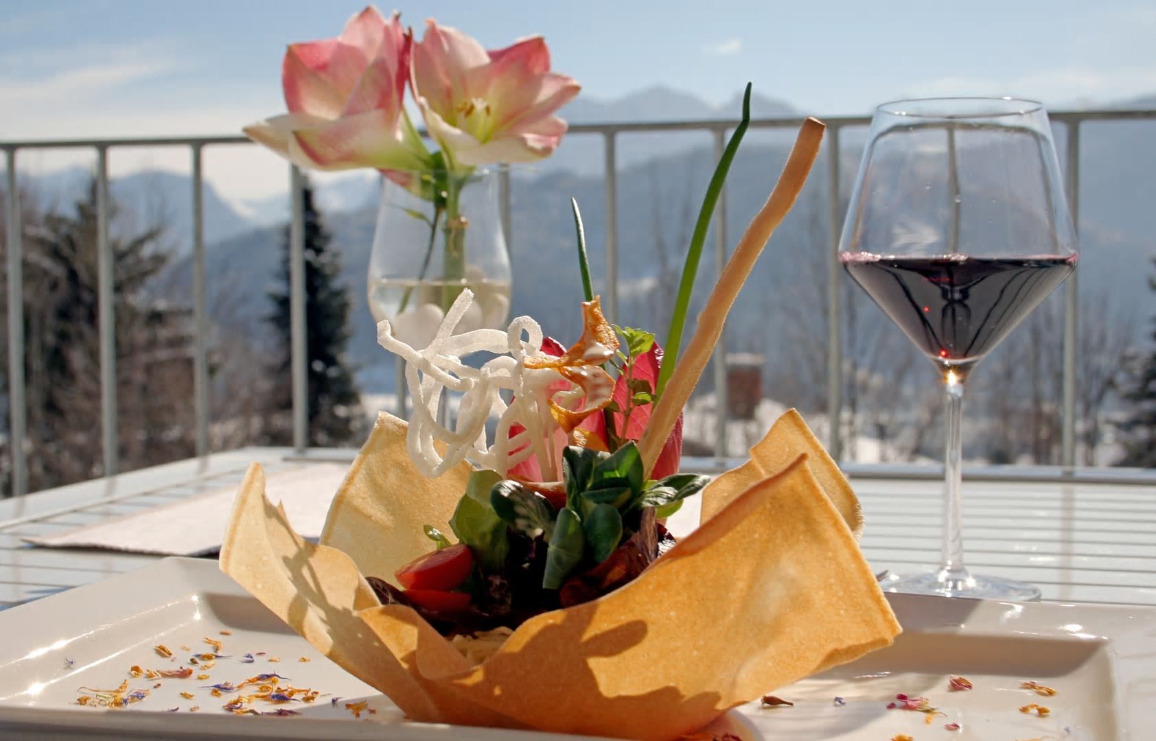 Een tafel met eten, een glas rode wijn en een vaas vol bloemen.