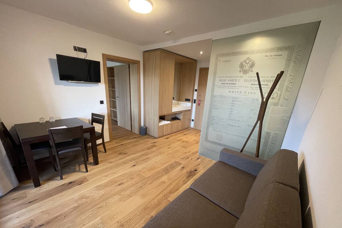 A compact living space with a dining area, a sofa, a television, and a wall-mounted certificate.