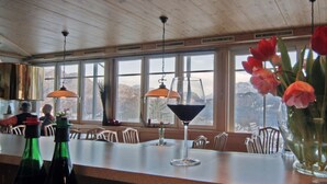 Un restaurante con techo de madera, ventanas amplias, zona de bar y un jarrón con flores en la barra.