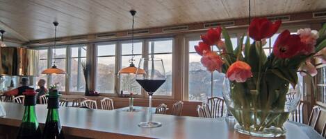 Un restaurante con techo de madera, ventanas amplias, zona de bar y un jarrón con flores en la barra.