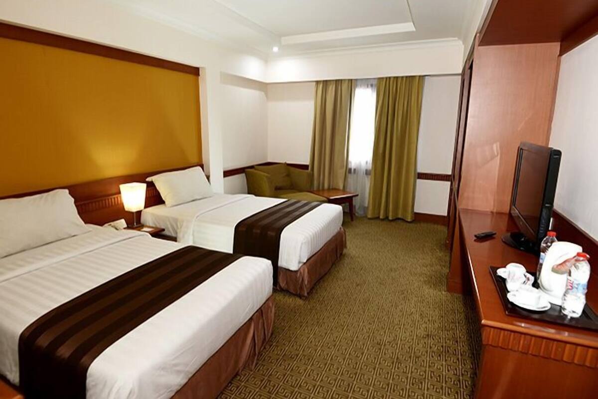 A hotel room with two beds, a desk with a television, and a window with curtains.