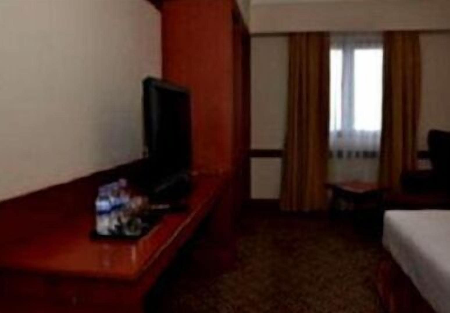 A hotel room with a wooden desk, a television, a bed, and a window with curtains.