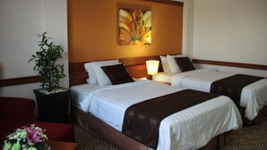 Une chambre d’hôtel avec deux lits, une table de chevet avec une lampe, une plante en pot et un arrangement floral.