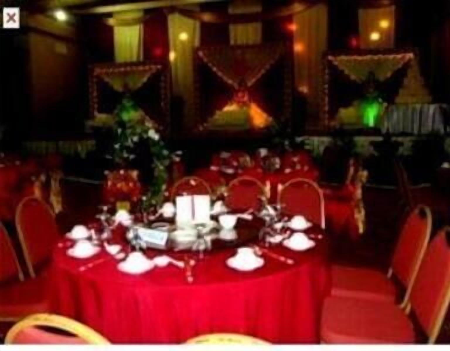 A dining area with round tables set for four, red tablecloths, and red chairs.