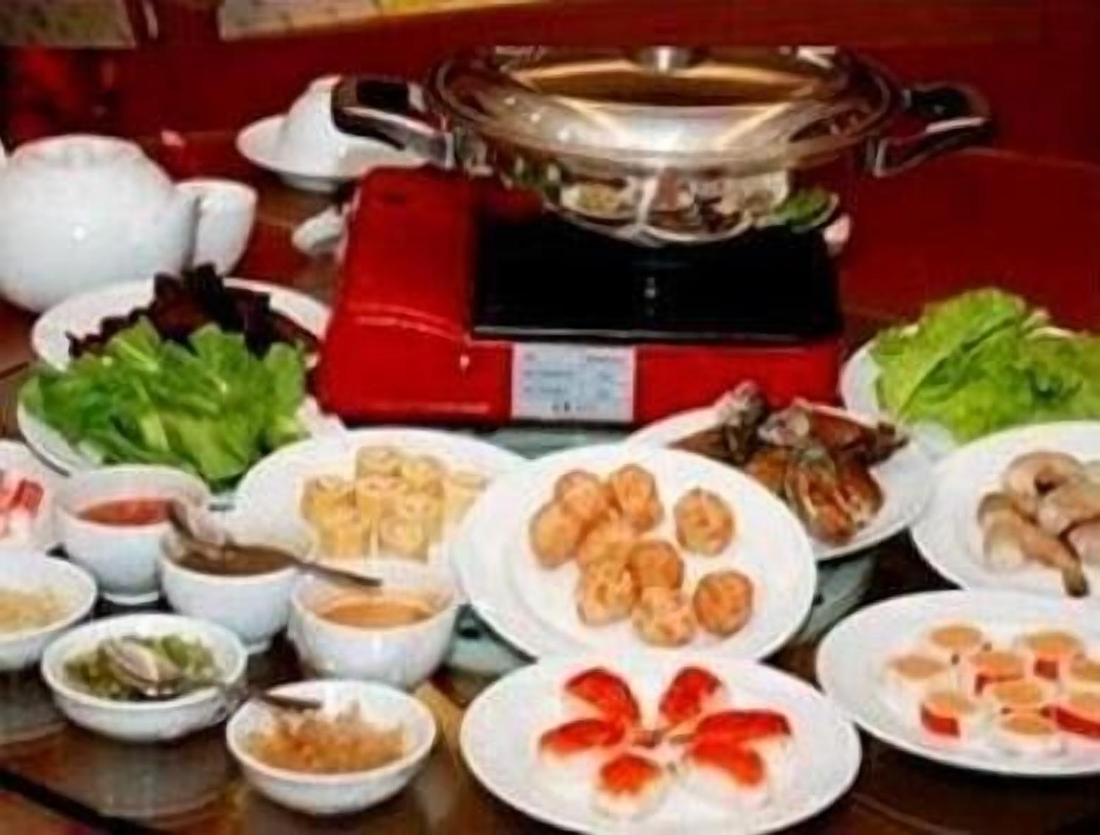 A table with various dishes including dumplings, vegetables, and a hot pot setup.