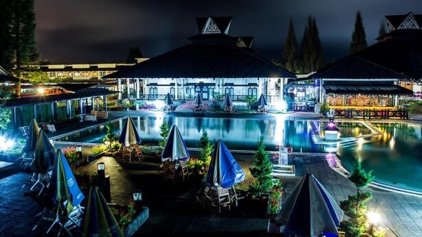 A nighttime view of a hotel with a swimming pool, outdoor seating, and covered areas.