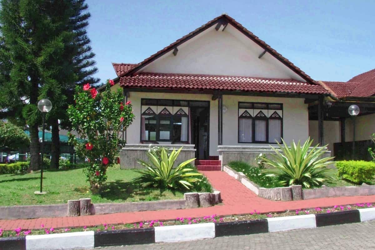 A two-story house with a tiled roof, a front porch, and a small garden with plants and flowers.
