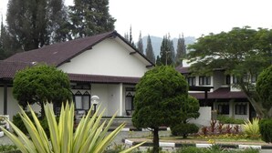 A building with a white facade and a red-tiled roof, surrounded by well-maintained gardens with various plants and trees.