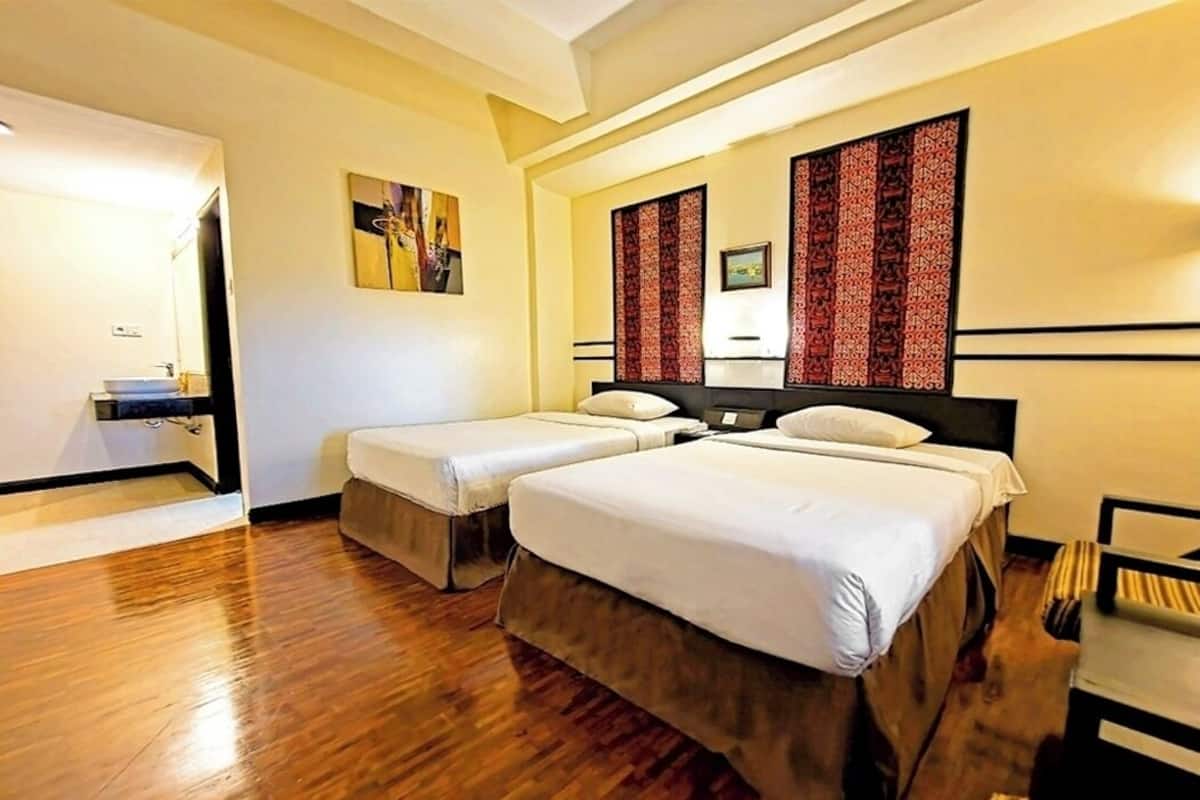 A hotel room with two beds, wooden flooring, a bathroom with a sink, and a mirror.