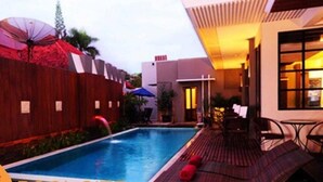 Une piscine dotée d’une terrasse en bois et de coins salon extérieurs, entourée d’une clôture en bois et agrémentée de parasols.