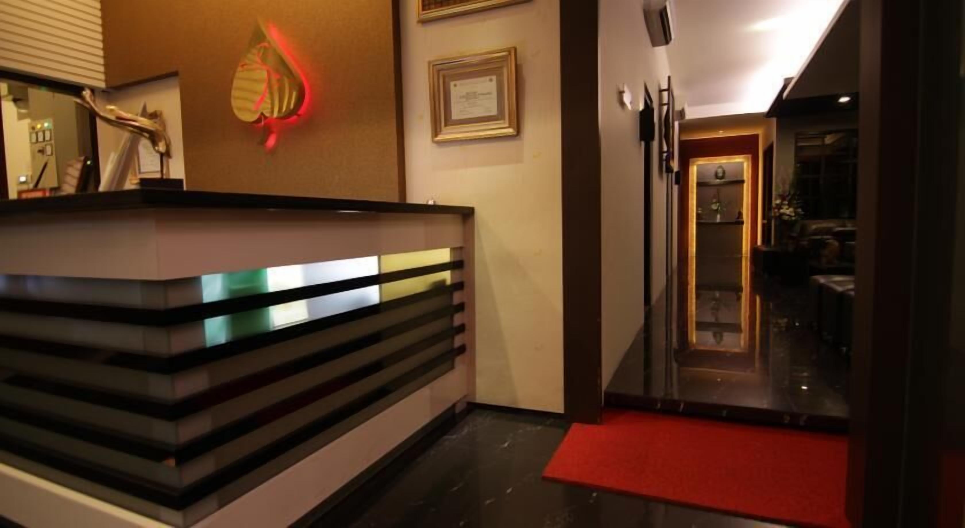 A reception area with a modern design, featuring a reception desk, a framed certificate on the wall, and a red carpet leading to a dining area.