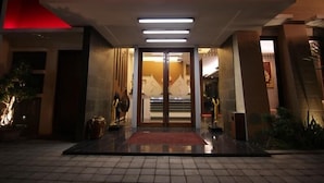 L’entrée d’un hôtel au design moderne, avec une porte en verre, un tapis rouge et un intérieur bien éclairé.